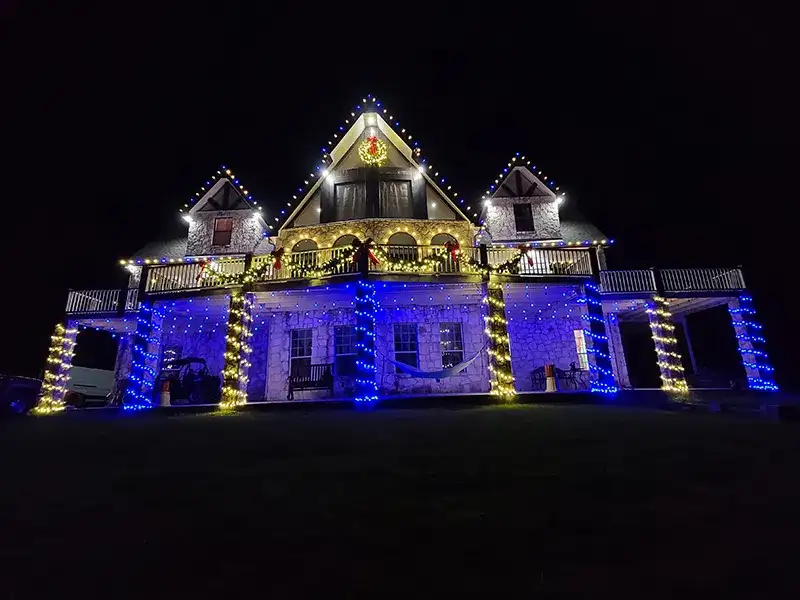 Large home with blue and gold lights wrapping the porch columns and railings