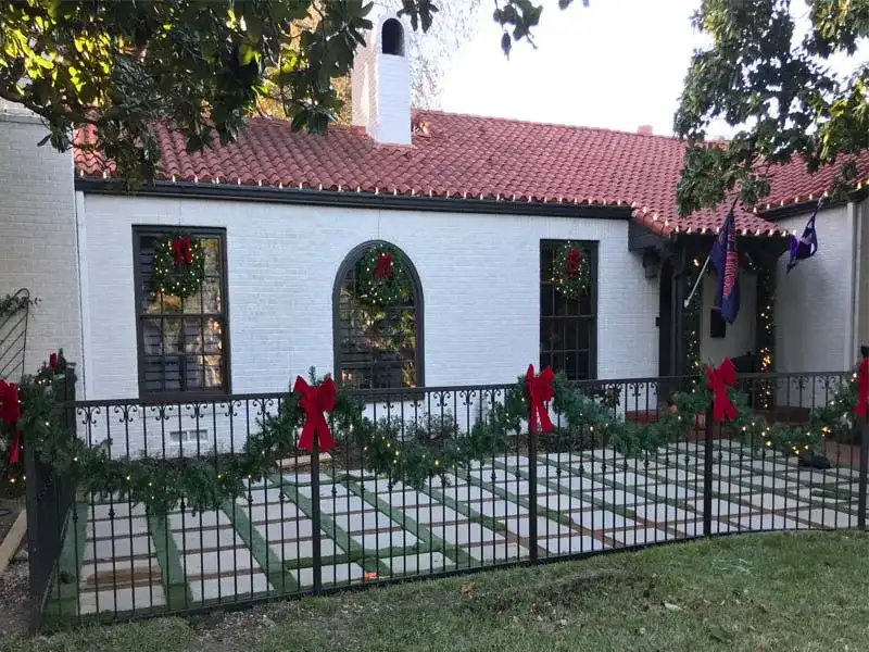 White stucco home with lit garland and red bows along the front fence