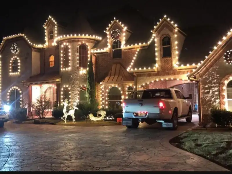 Large stone home outlined in warm white lights with a lit tree